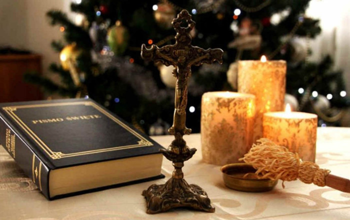 Pismo święte, krzyż i świece na stole. W tle choinka, drzewko będące ozdobą w czasie świąt Bożego Narodzenia